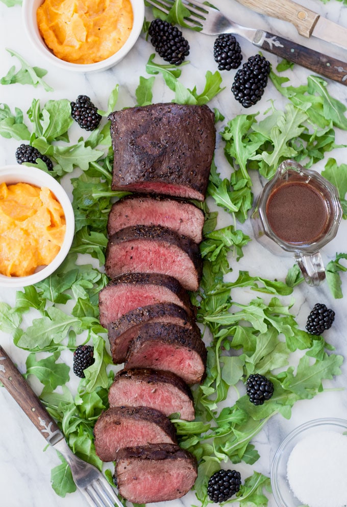 sliced venison loin with blackberry sauce on a bed of arugula