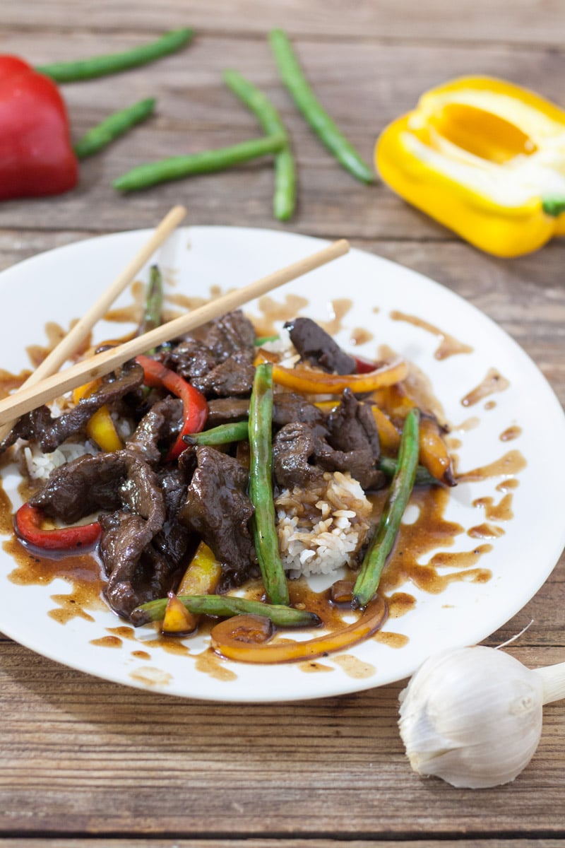 Venison teriyaki on white plate with red and yellow peppers and green beans