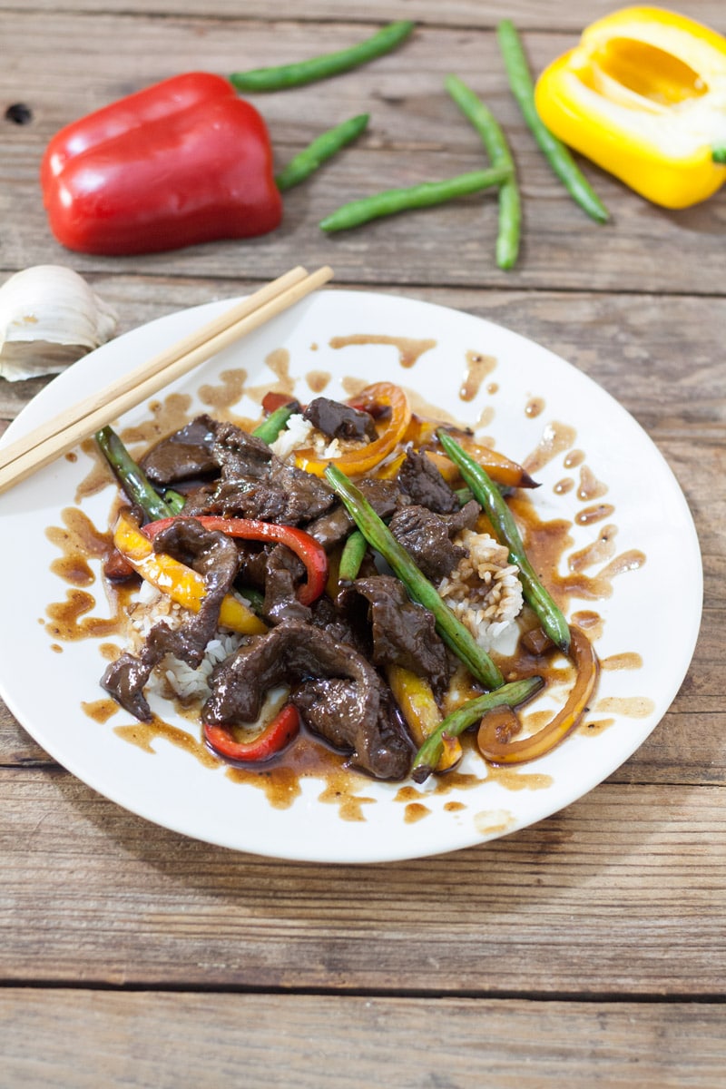 Venison teriyaki on white plate with red and yellow peppers and green beans