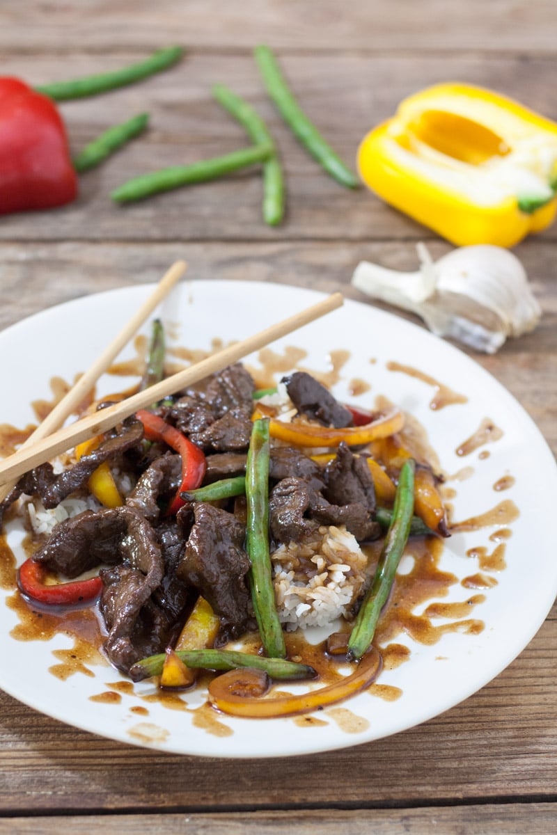 Venison teriyaki on white plate with red and yellow peppers and green beans