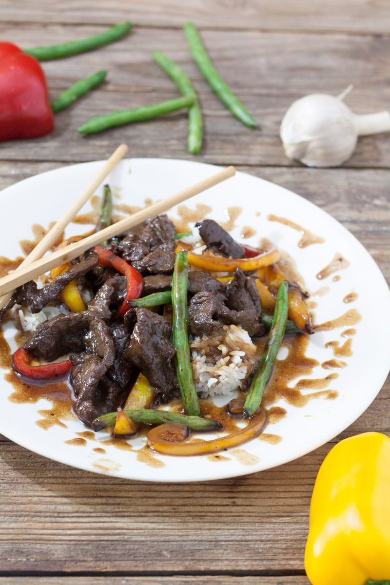 Venison teriyaki on white plate with red and yellow peppers and green beans