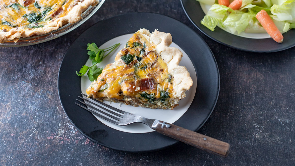Slice of quiche with whole onion spinach quiche and side salad.