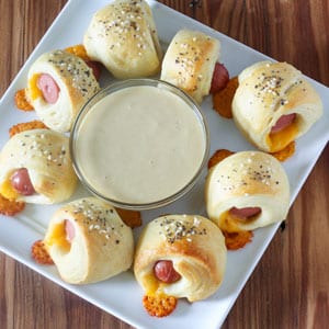 pigs in a blanket with honey mustard dipping sauce on square white plate