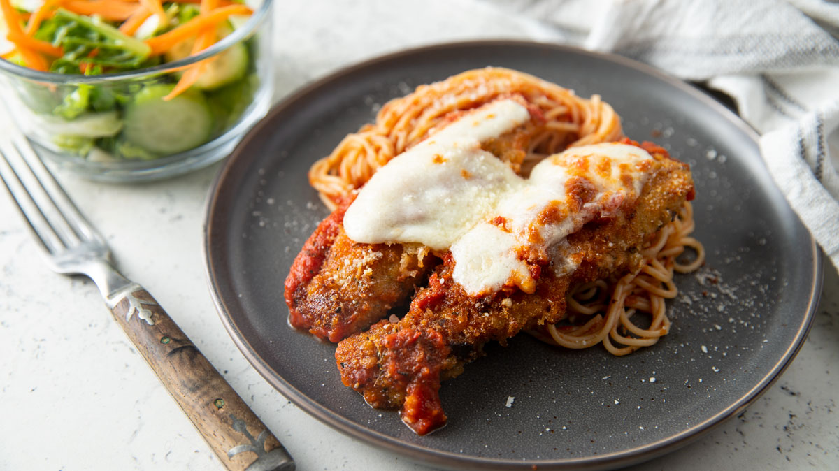 Cheese topped fried rabbit loin on a bed of pasta.