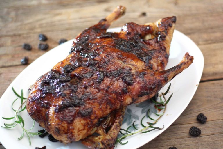 Balsamic Cherry Glazed Whole Duck on a platter with rosemary sprigs and dried cherries