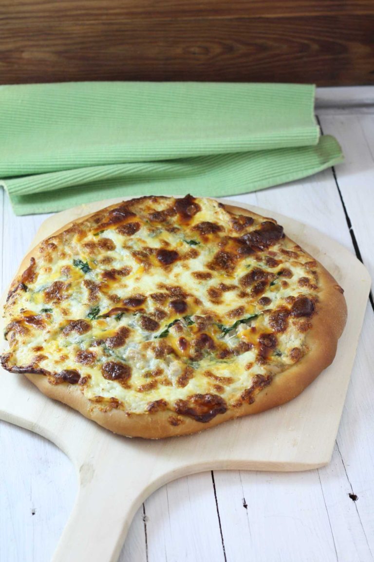 Tuna Florentine Pizza with Lemon, dill aioli on a wooden pizza peel near a light green tea towel
