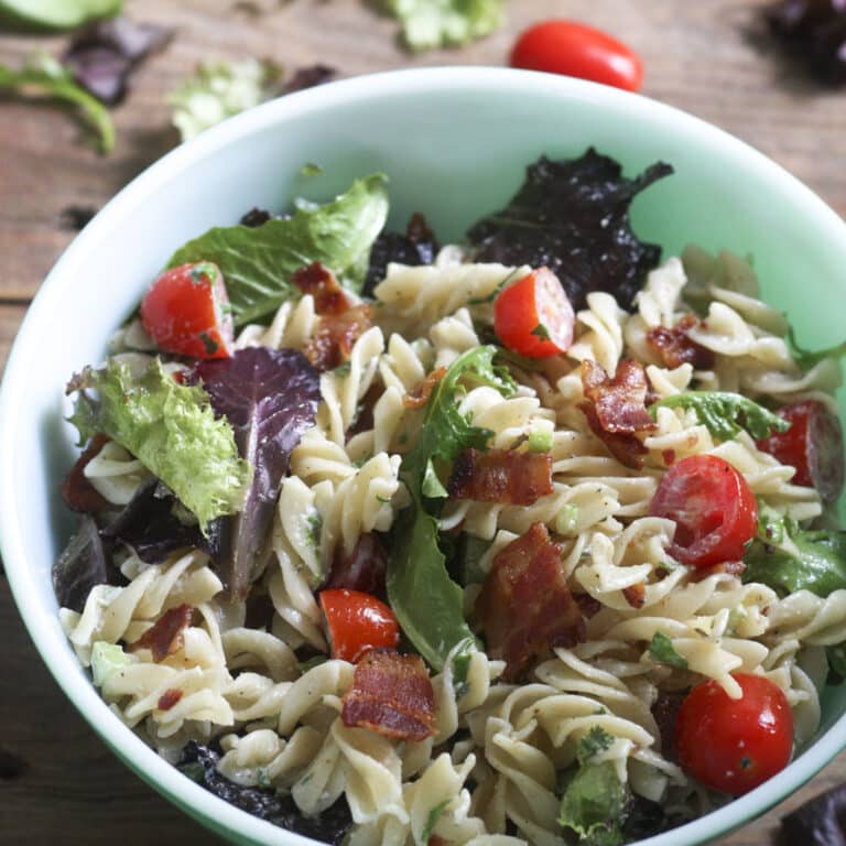 blt pasta salad in green bowl on wooden board