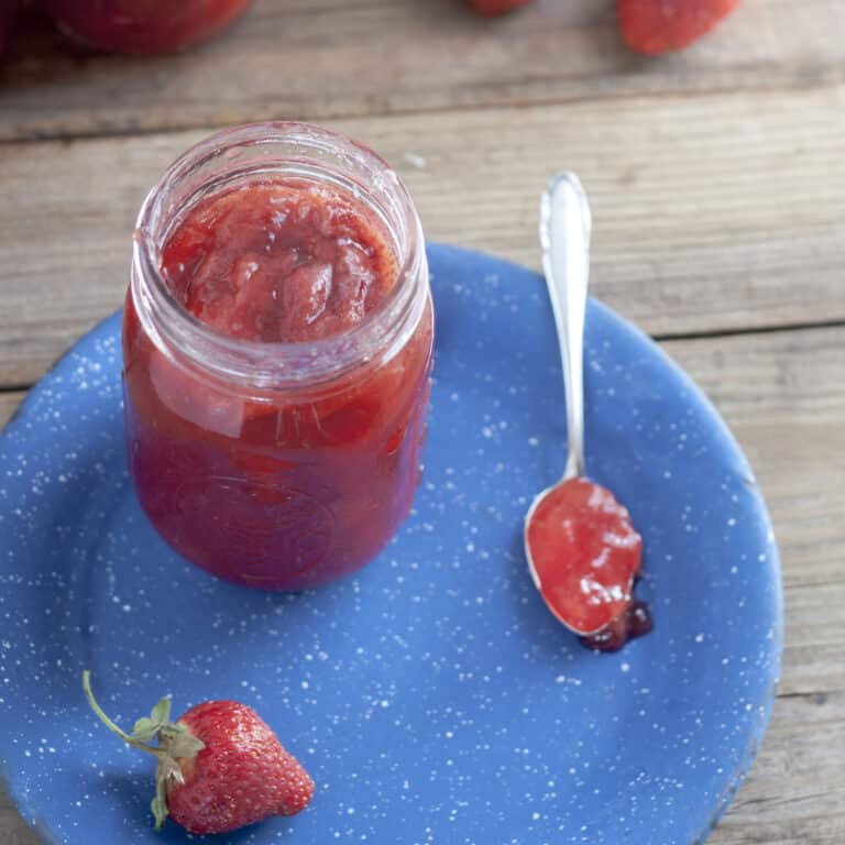 strawberry jam in canning jar with spoon and blue plate