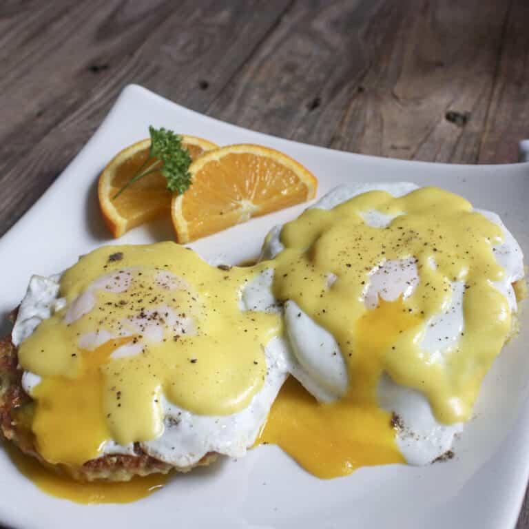 eggs benedict on white plate with broken yolks