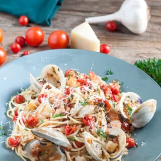 Seafood Fra Diavolo Whole clams with shells, chunks of whole bay scallops and burst cherry tomatoes on a bed of pasta