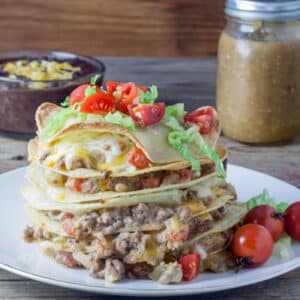 Large stack of tortillas with meat and cheese between each layer topping with shrdded lettuce and diced cherry tomatoes