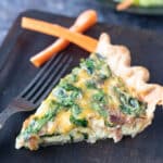Slice of quiche on wooden plate.