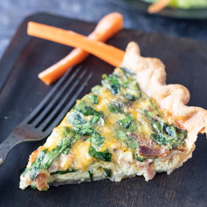 Slice of quiche on wooden plate.