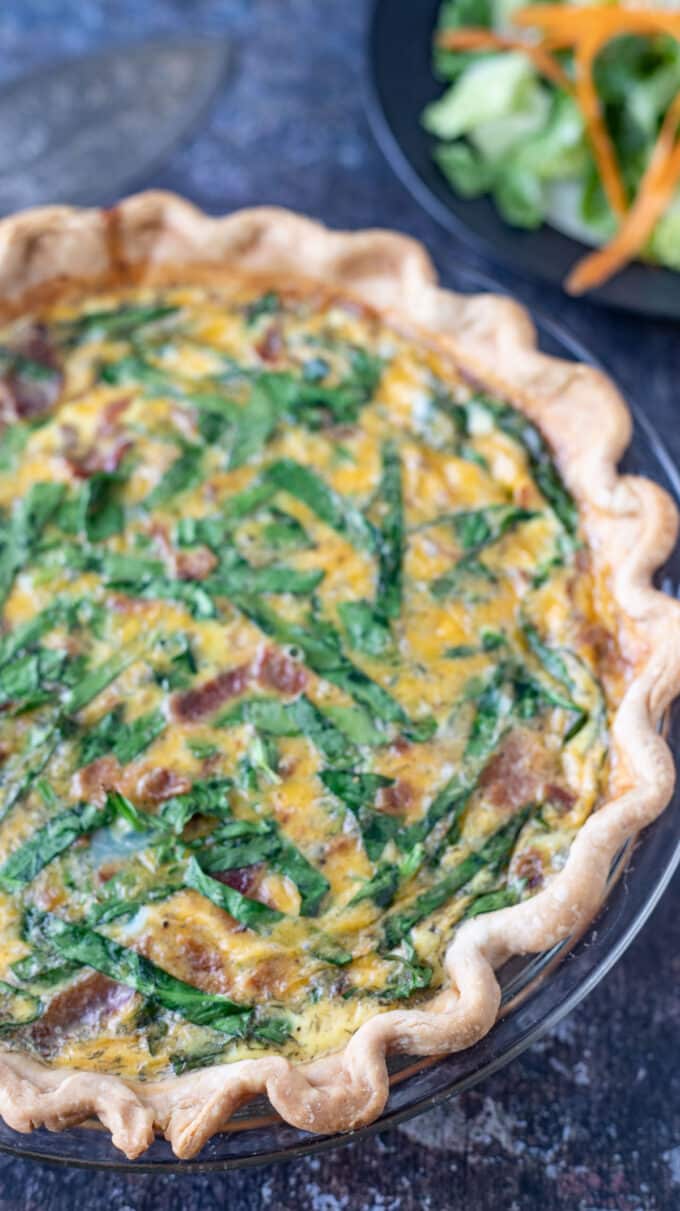 Whole quiche on a black board with side salad.