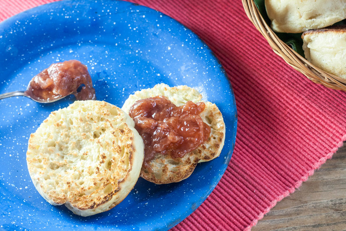 Toasted english muffin and silver spoon of jam on blue plate