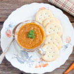 Small cup of carrot soup on a white plate with orange flowers.