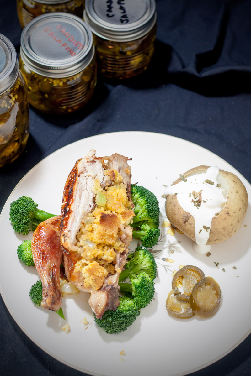 Half Cornish game hen stuffed with cornbread & sausage stuffing with broccoli and baked potato with sour cream on white plate