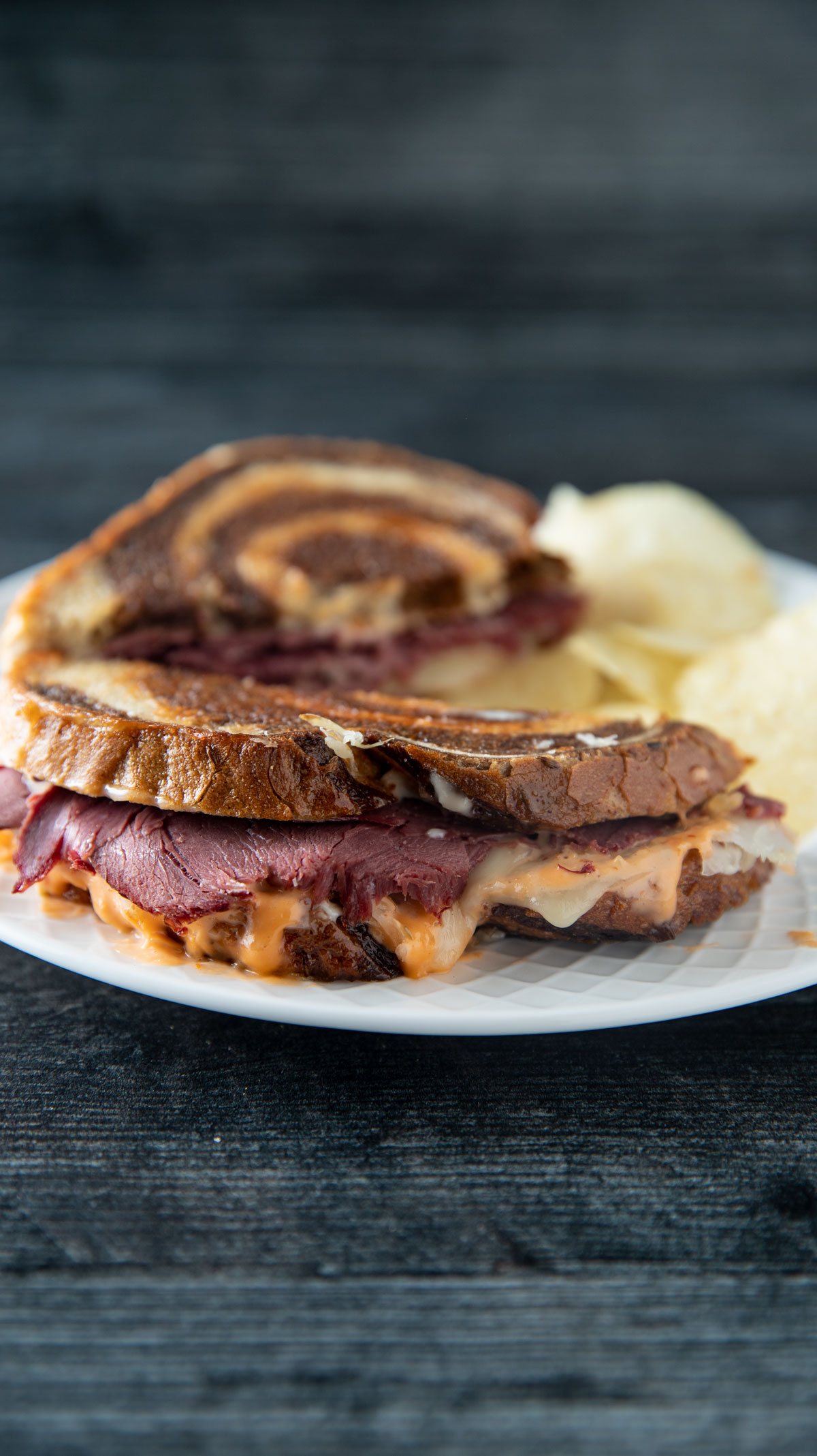Venison reuben Sandwich on a white plate with potato chips.
