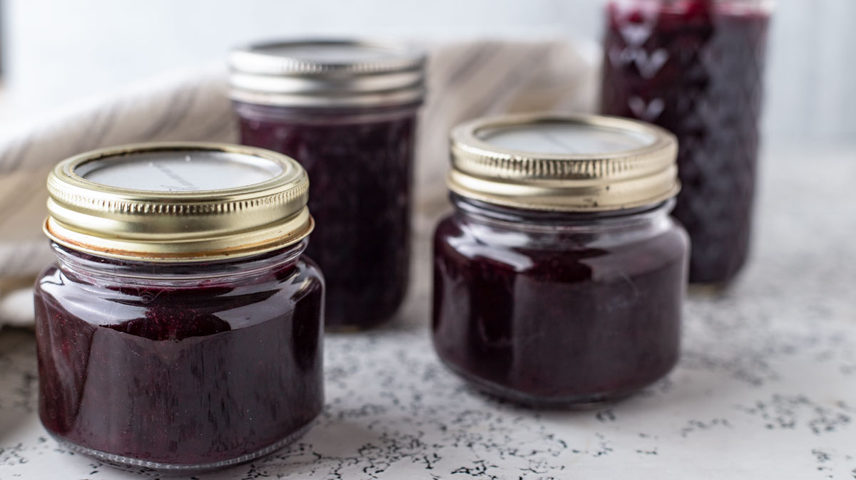 Jars of blueberry jam on white board.