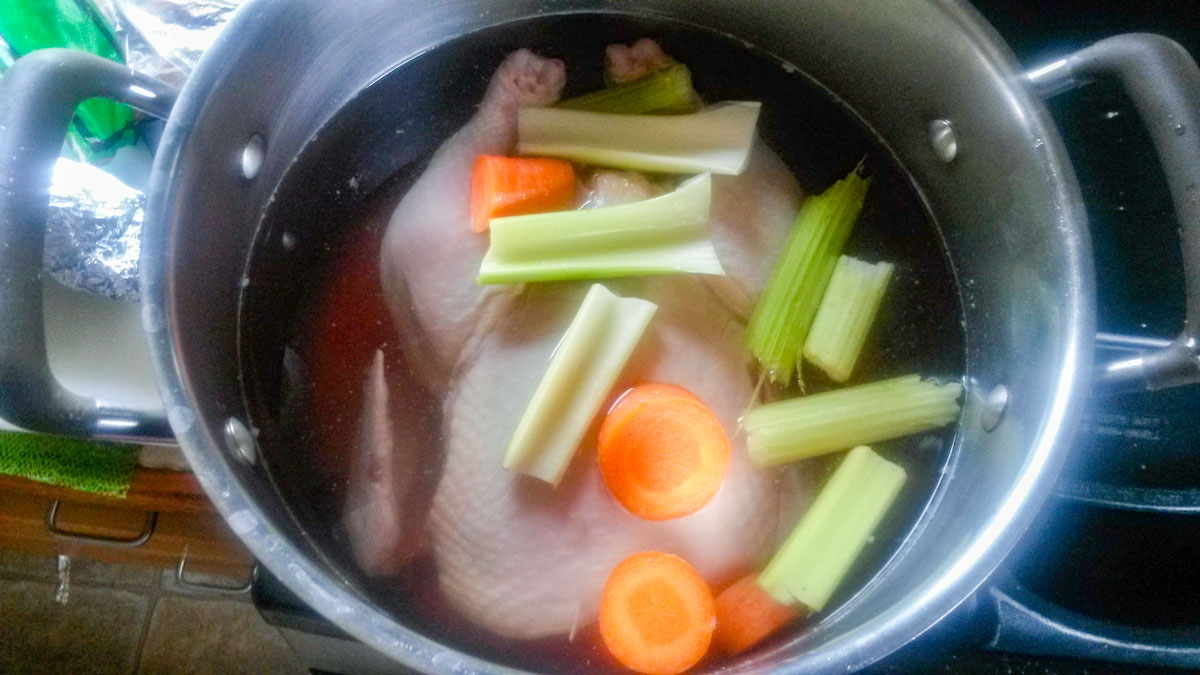 Whole chicken in a pot with carrots and celery.