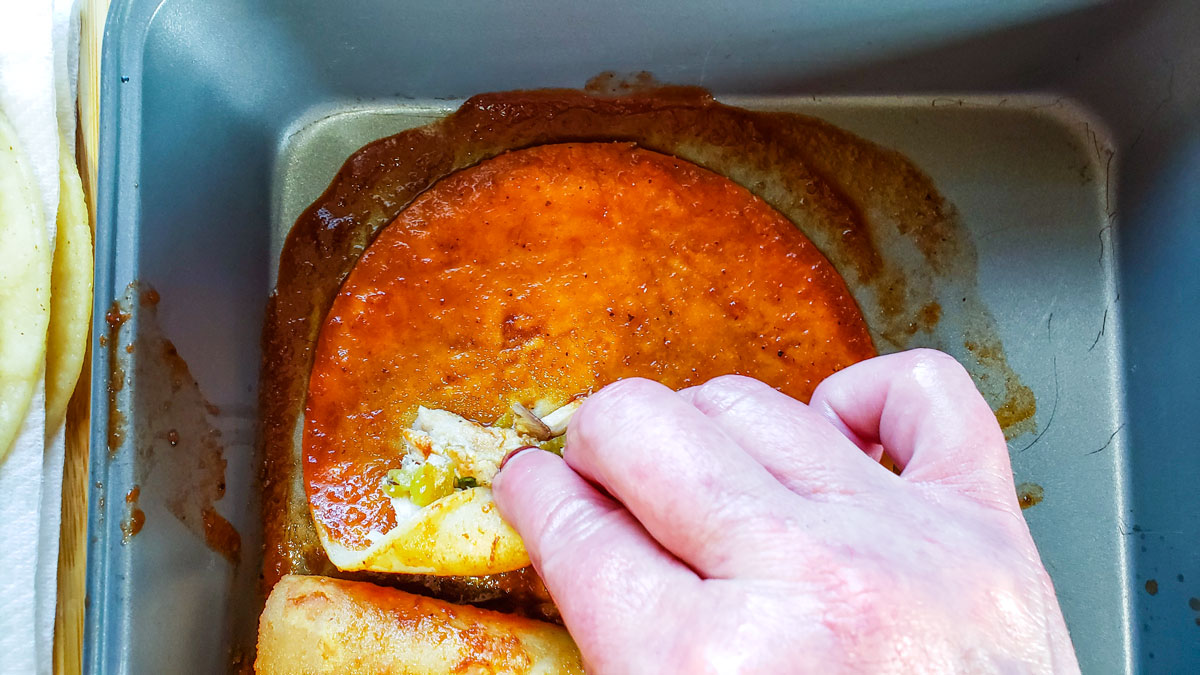 Filled enchilada with women's hand rolling up the tortilla.