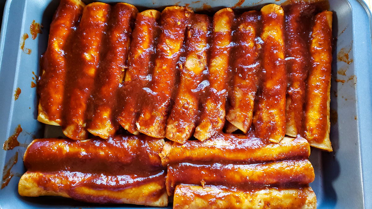 Enchiladas added to a baking pan. More sauce spread over the pan.