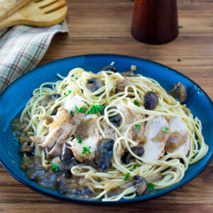 Blue plate filled with chicken marsala topped spaghetti.