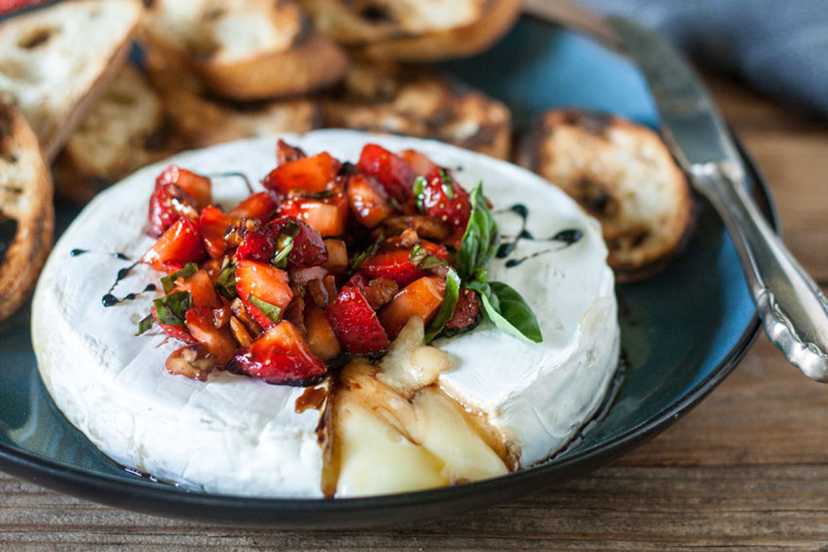 Sliced brie and strawberries with chees oozing onto plate.