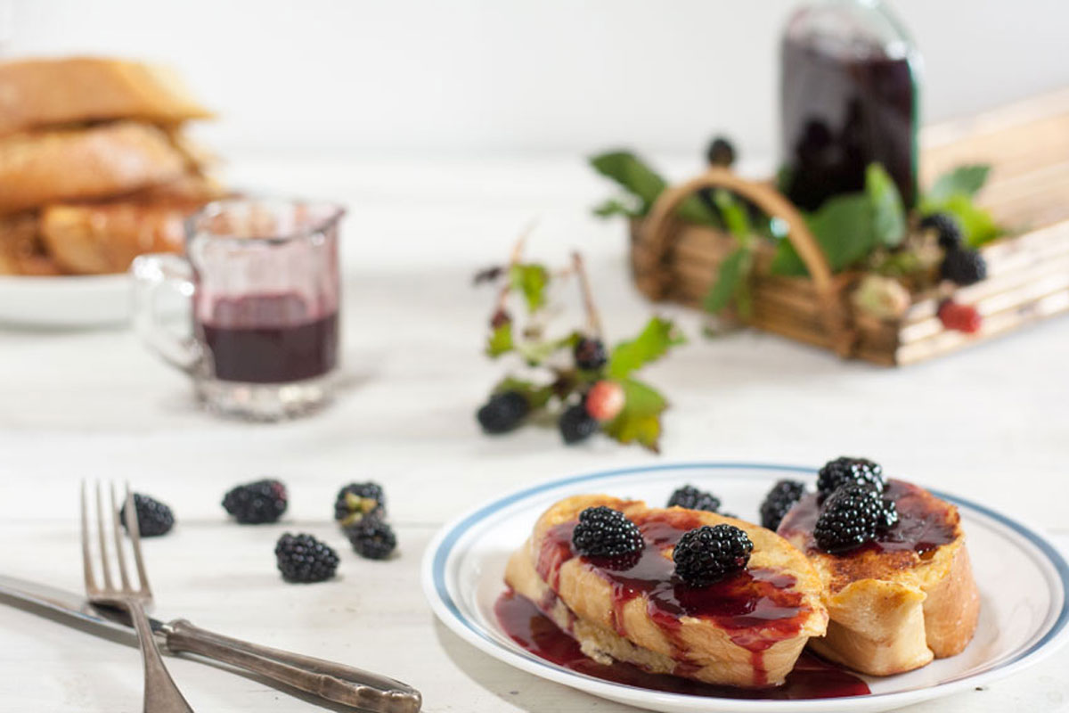 White plate with french toast topped with blackberry syrup and fresh blackberries