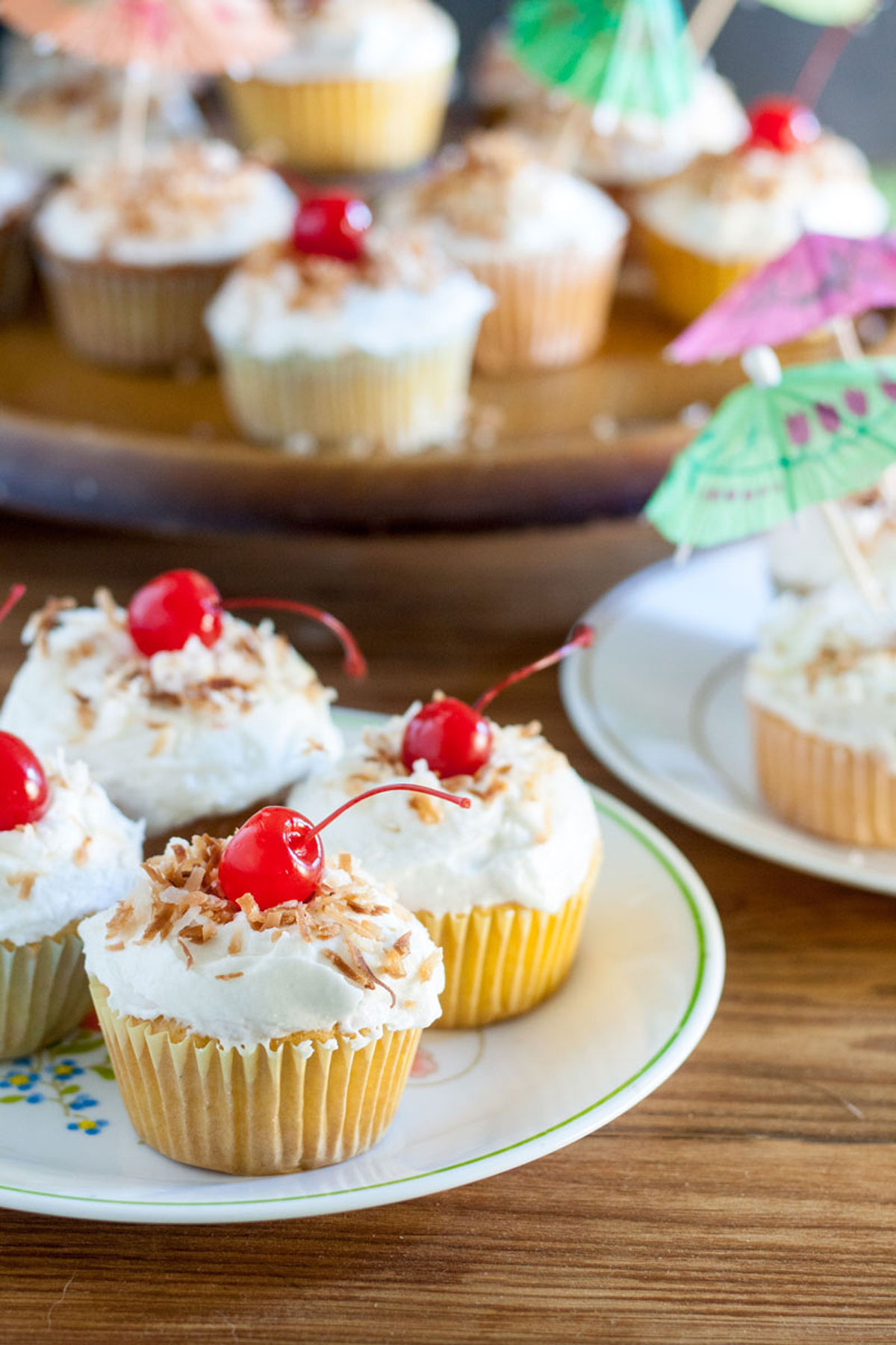 4 pina colada cupcakes on white plate garnished with toasted coconut and maraschino cherry 4 pina colada cupcakes on white plate garnished with toasted coconut and maraschino cherry