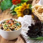 Roasted corn and black bean salsa in a beige bowl with chips and sunflowers in the background.