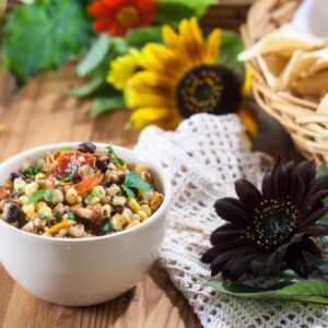Roasted corn and black bean salsa in a beige bowl with chips and sunflowers in the background.