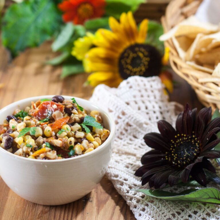 Roasted corn and black bean salsa in a beige bowl with chips and sunflowers in the background.