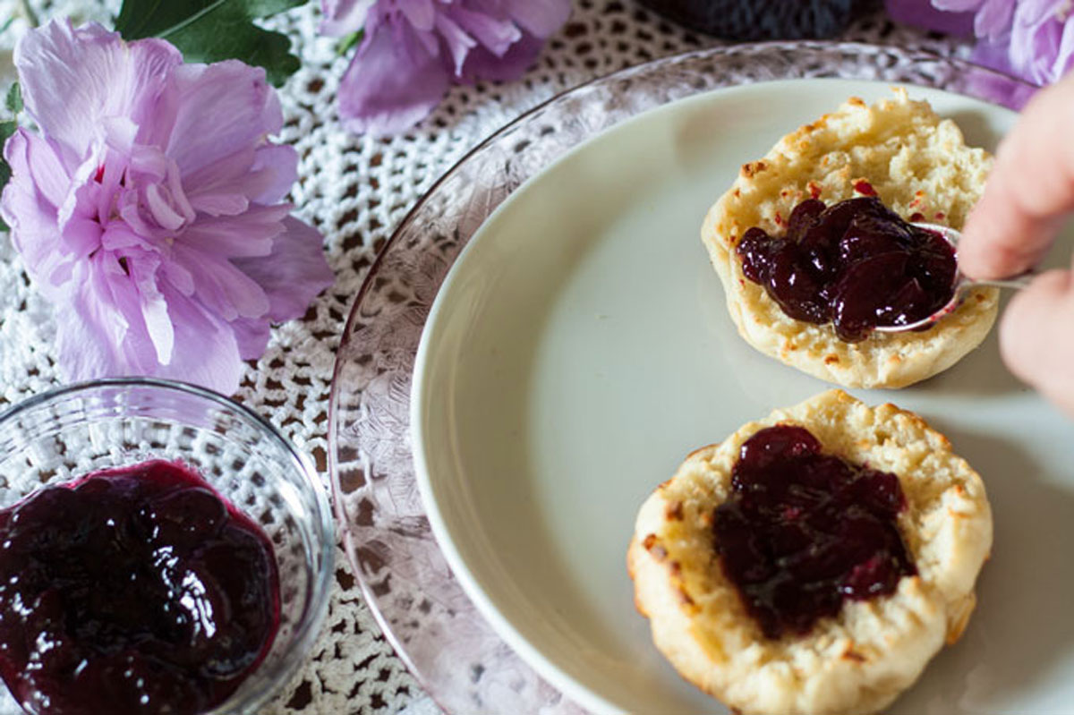 Blackberry jam on muffin with jars of jam.