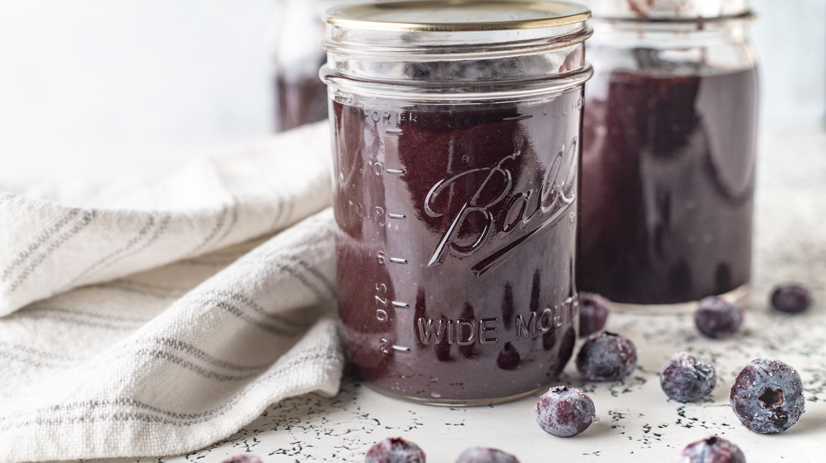 Two jars of blueberry BBQ sauce on a white board.