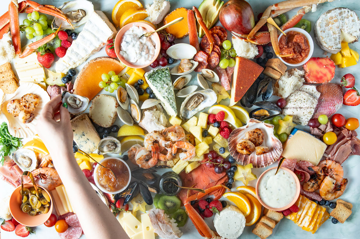 Woman's hand grabbing an oyster from a large charcuterie board.