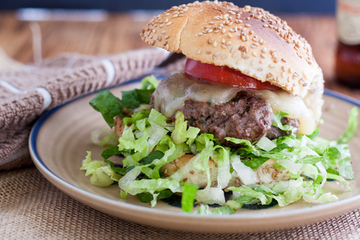 Venison cheeseburger topped with thick sliced tomato on poppy seed bun
