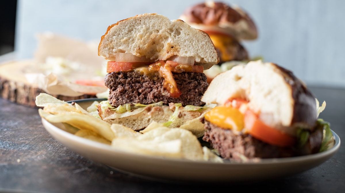 Medium rare venison burger cut in half on pretzel bun.