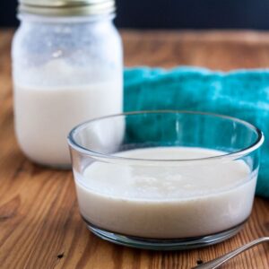 Clear glass bowl with evaporated milk with a jar and green tea towel in the background.