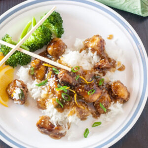 Sesame chicken over steamed rice with broccoli and orange wedges.