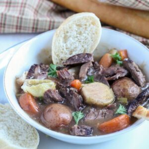 White bowl filled with rustic venison neck roast stew with a slice of bread.
