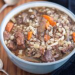 Gray bowl filled with hearty venison soup with vegetables and barley.