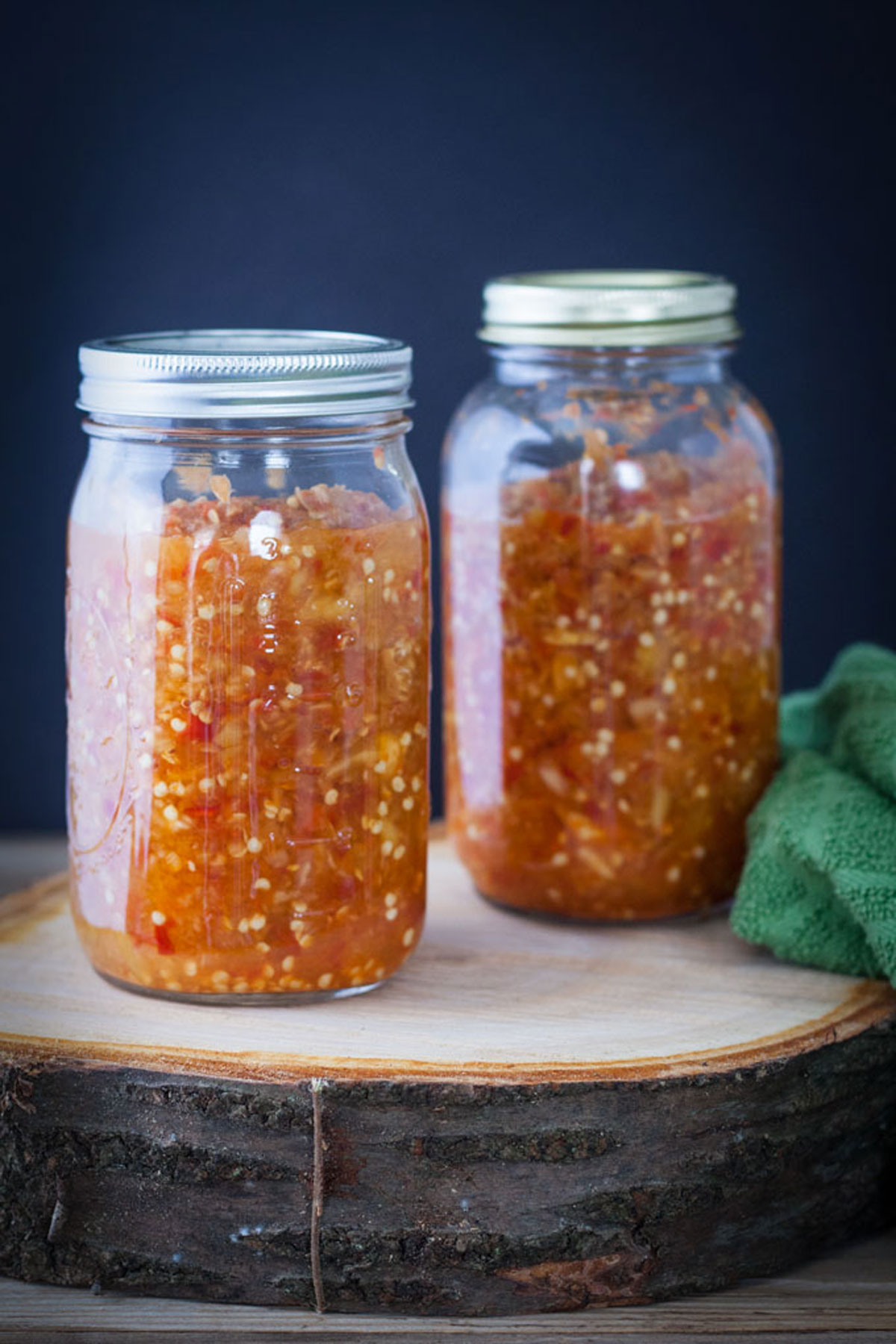Two jars of fermented peppers on tree slab.