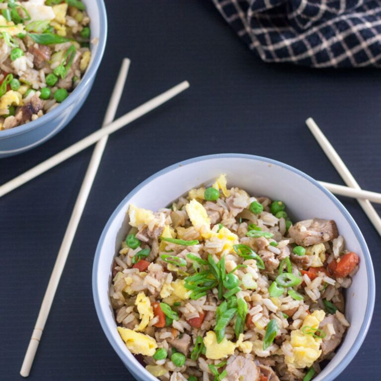 Grey bowl with colorful fried rice with vegetables and scrambled egg, garnished with green onion.