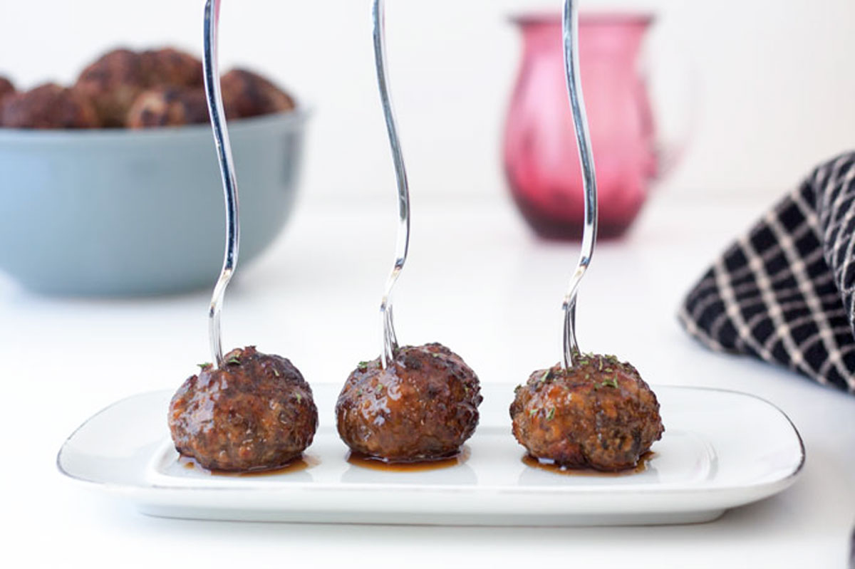 Three meatballs on white tray with forks sticking out.