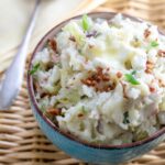 Blue bowl filled with colcannon mashed potatoes and cabbage garnished with melted butter and bacon bits.