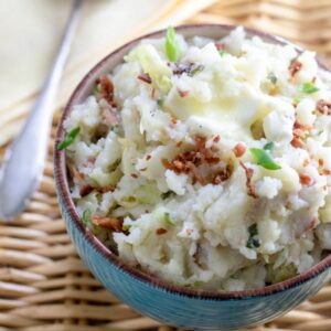 Blue bowl filled with colcannon mashed potatoes and cabbage garnished with melted butter and bacon bits.