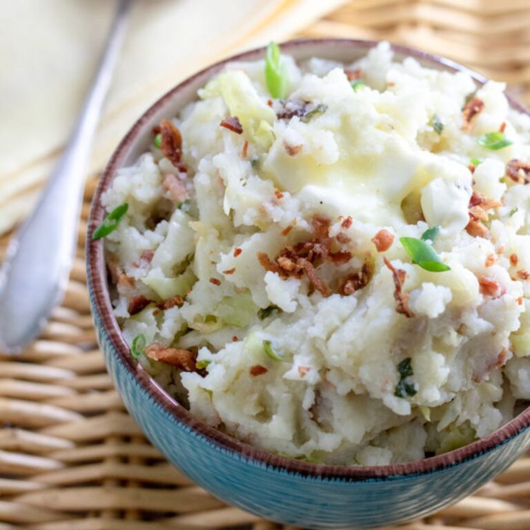 Blue bowl filled with colcannon mashed potatoes and cabbage garnished with melted butter and bacon bits.