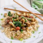 White plate filled with cahew pork stir fry atop a bed of rice.