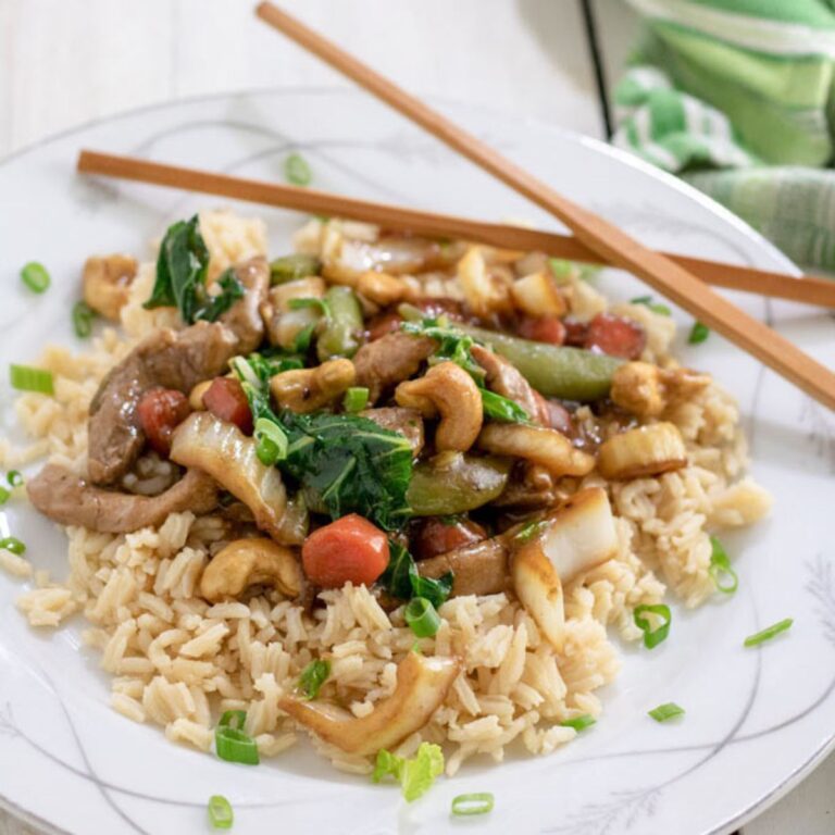 White plate filled with cahew pork stir fry atop a bed of rice.